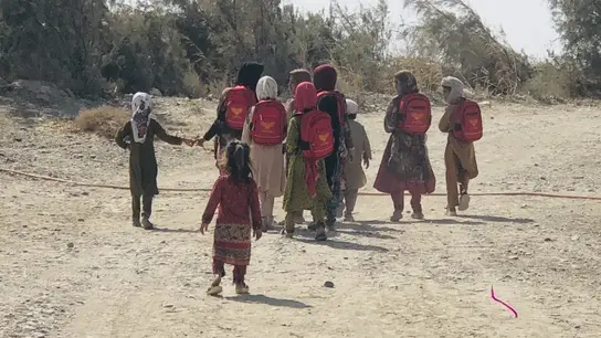 Los niños con mochilas rojas van por un camino polvoriento a lo largo de una zona rural en su camino a la escuela.