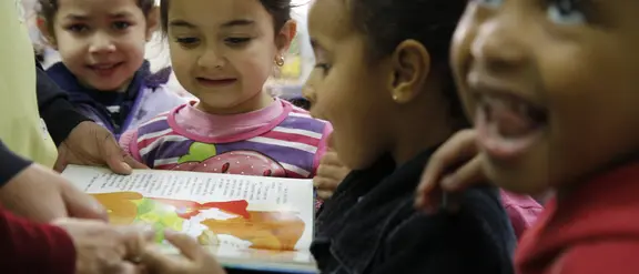  Kinder betrachten neugierig ein Bilderbuch, das von einem Erwachsenen gehalten wird, und zeigen Begeisterung für das Lesen.