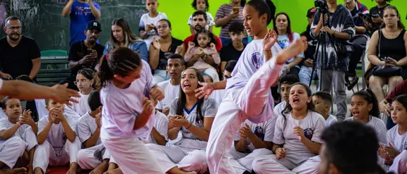 Zwei Kinder beim Kampfsport. Im Hintergrund schauen Kinder zu
