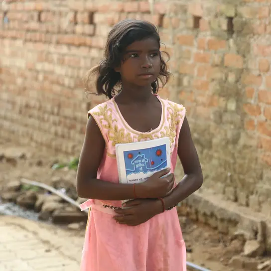 Indien: Das Mädchen Suniti hält ein Buch auf dem Weg zur Schule.