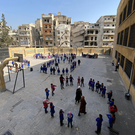 Kinder spielen auf einem Pausenhof zwischen zerstörten Gebäuden in Aleppo.